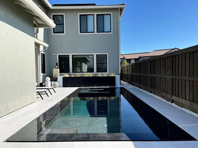 Sleek modern pool with dark tile alongside contemporary home