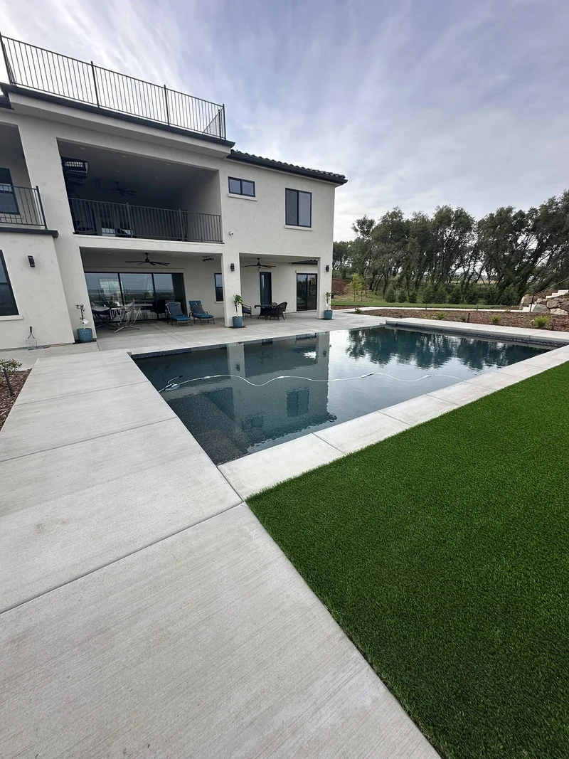 Modern home with a dark-tile pool, wide concrete deck, and turf inlays
