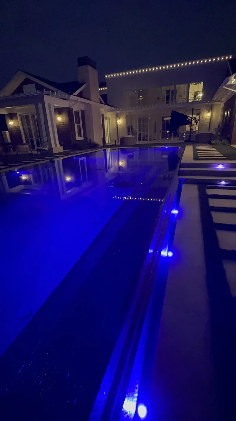 Aerial night view of a glowing blue pool and illuminated yard