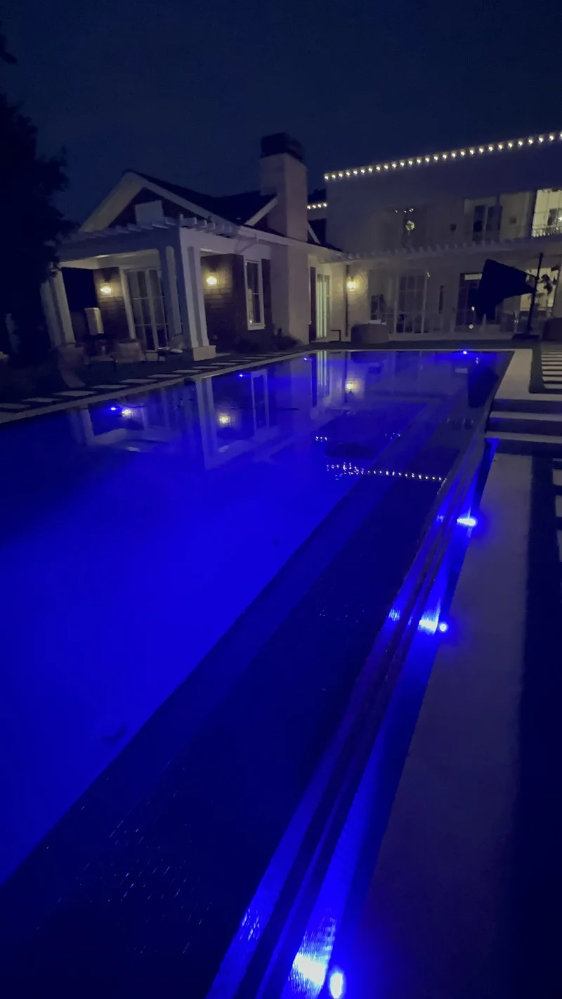 Pool glowing with blue LED lighting beside a modern home at night
