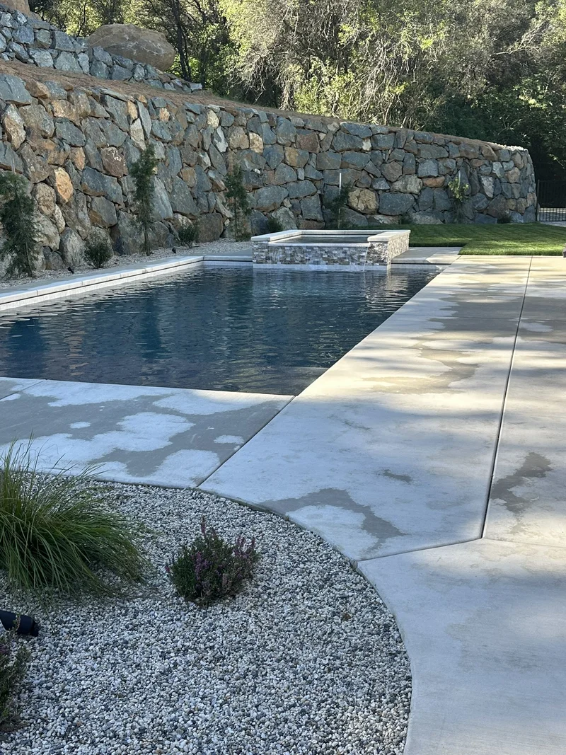 Stacked-stone wall framing a concrete pool deck and raised spa
