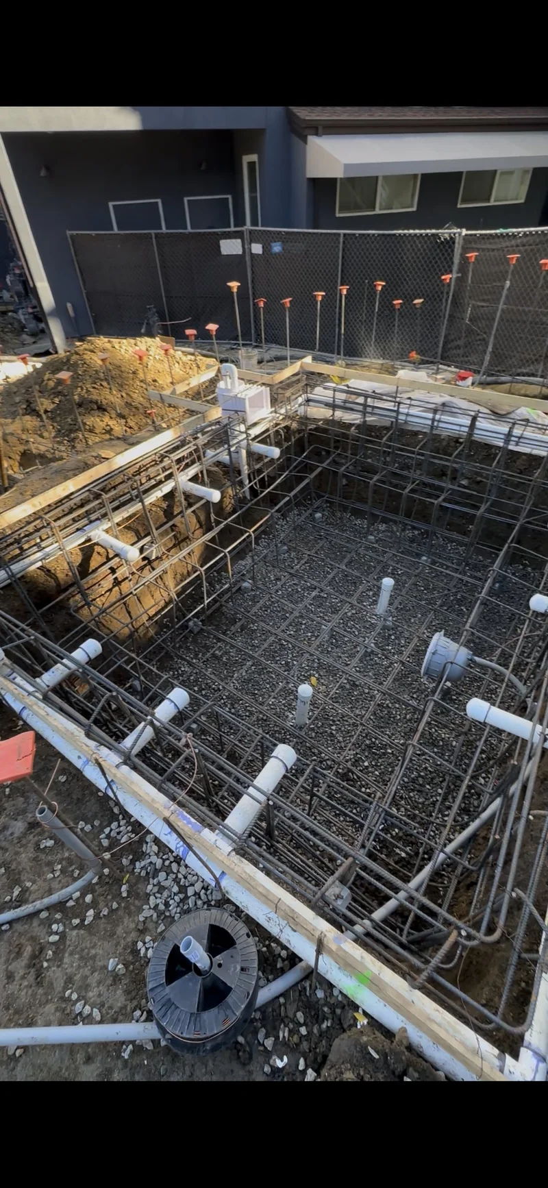 Steel reinforcement and plumbing rough-in inside a pool excavation during construction